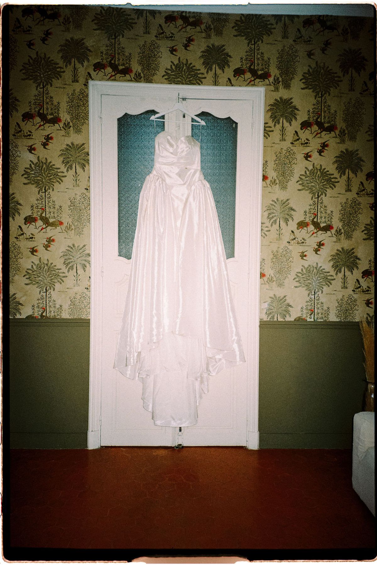 Clara's wedding dress hangs against the patterned wallpaper before she puts it on