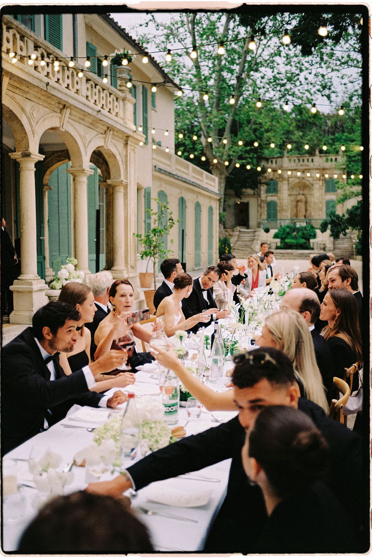 Guests raise their glasses along the long reception table under the string lights