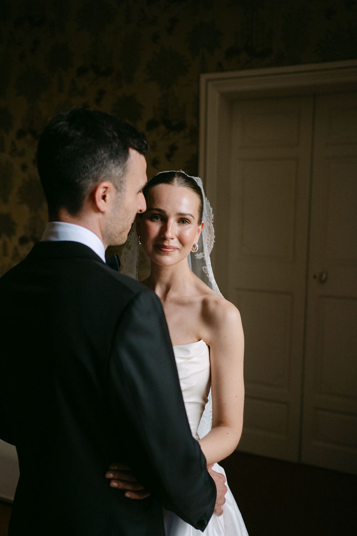 Clara and Constantin stand face to face outdoors, her veil catching the light