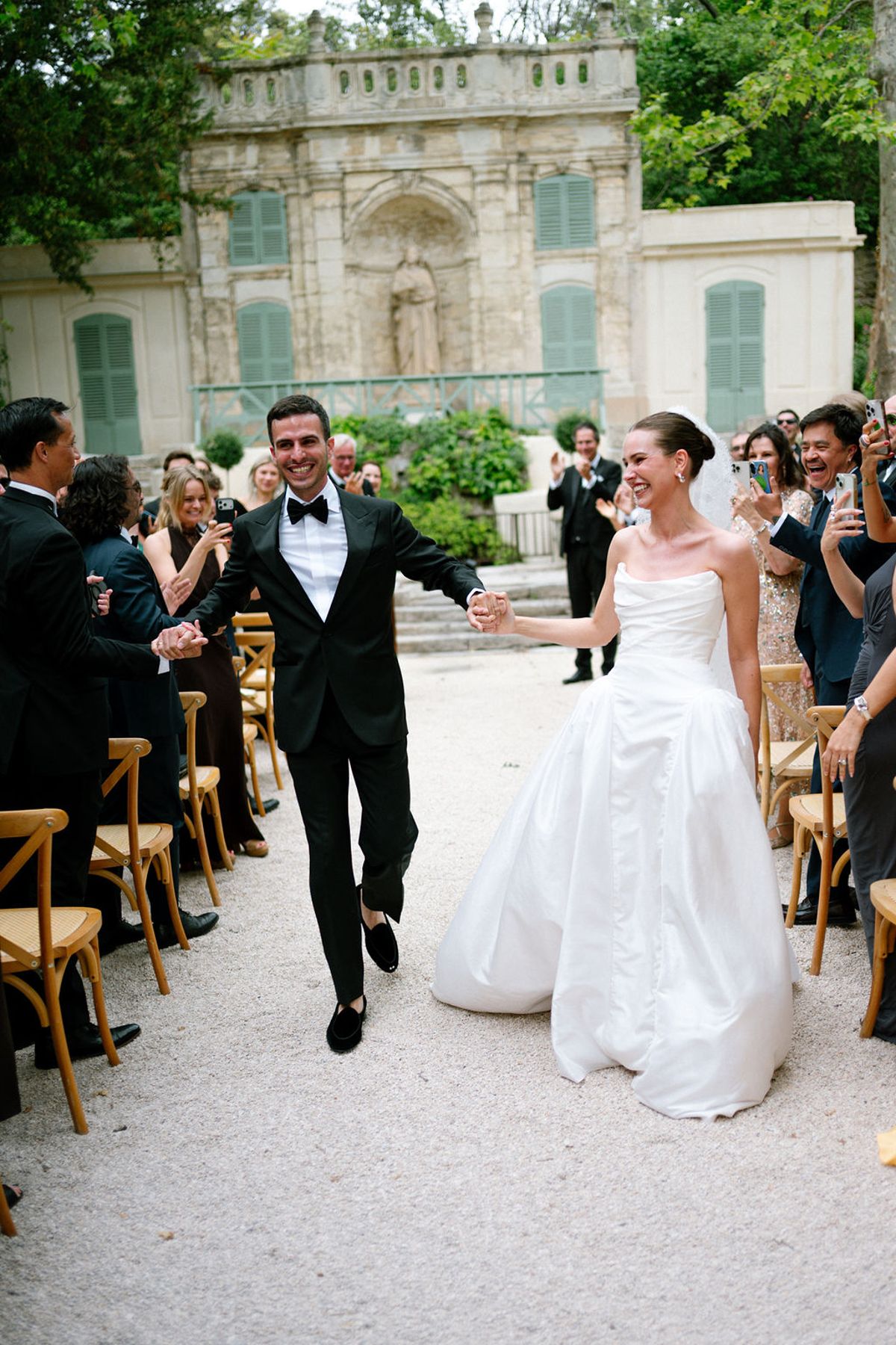 Clara and Constantin walk together as seated guests applaud on either side