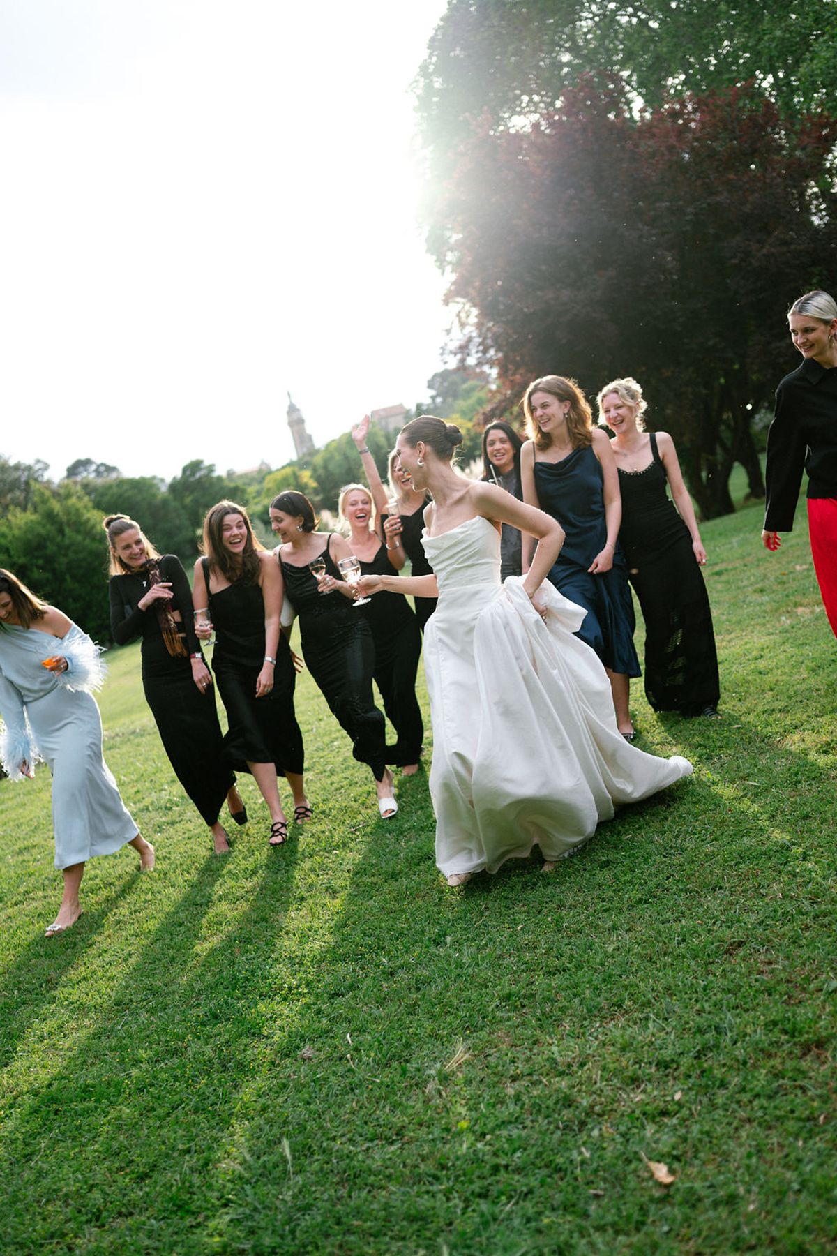 Clara walks across the lawn with her bridesmaids in black dresses, laughing