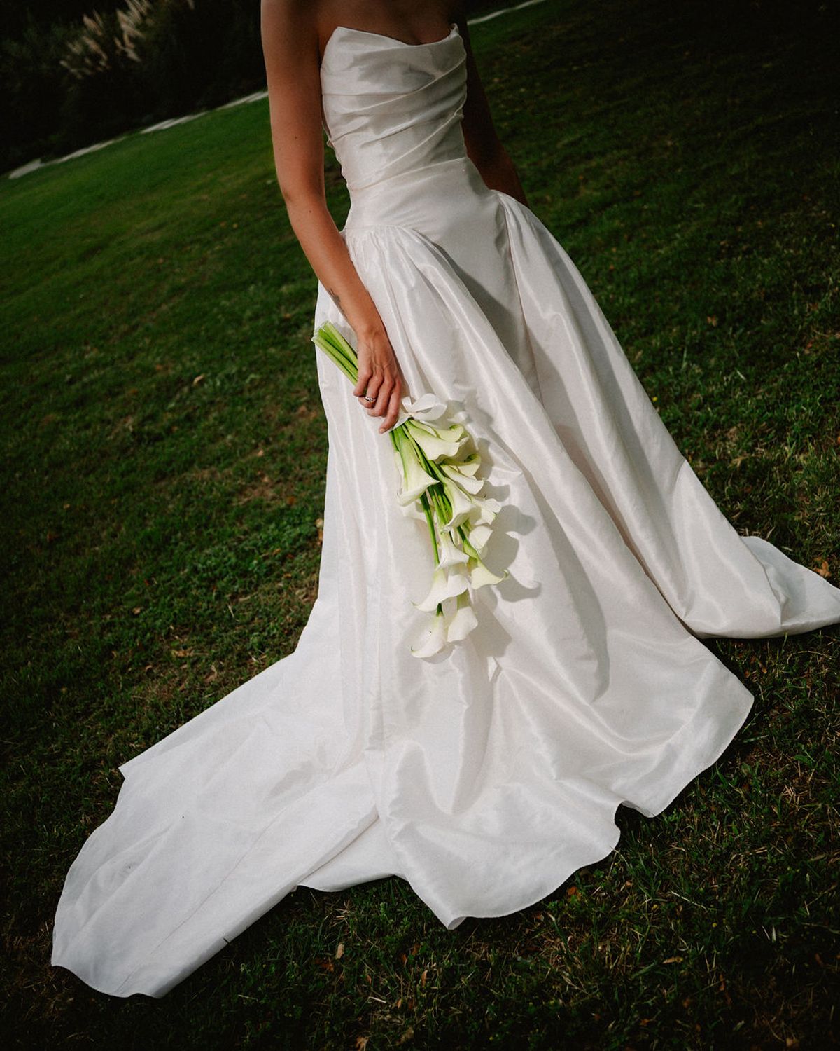 Clara lifts the train of her wedding dress, calla lilies in hand
