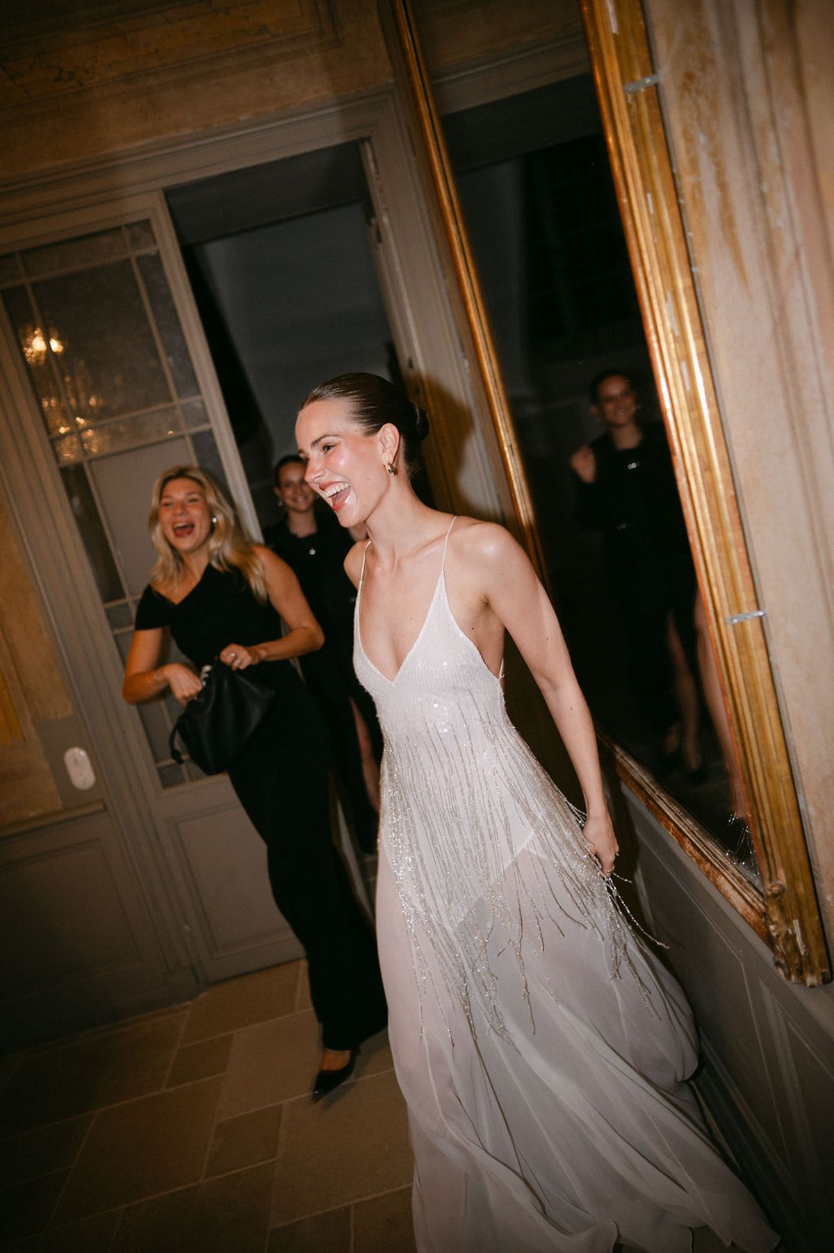 Clara crosses a doorway in a gold slip dress during the evening celebrations