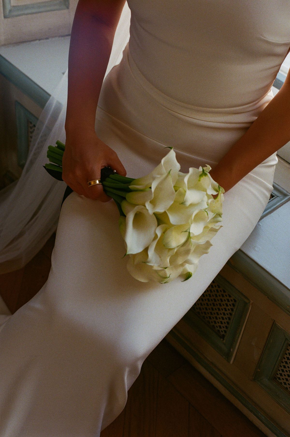A close view of the bride's fitted ivory dress and her hands holding a bouquet of white calla lilies.