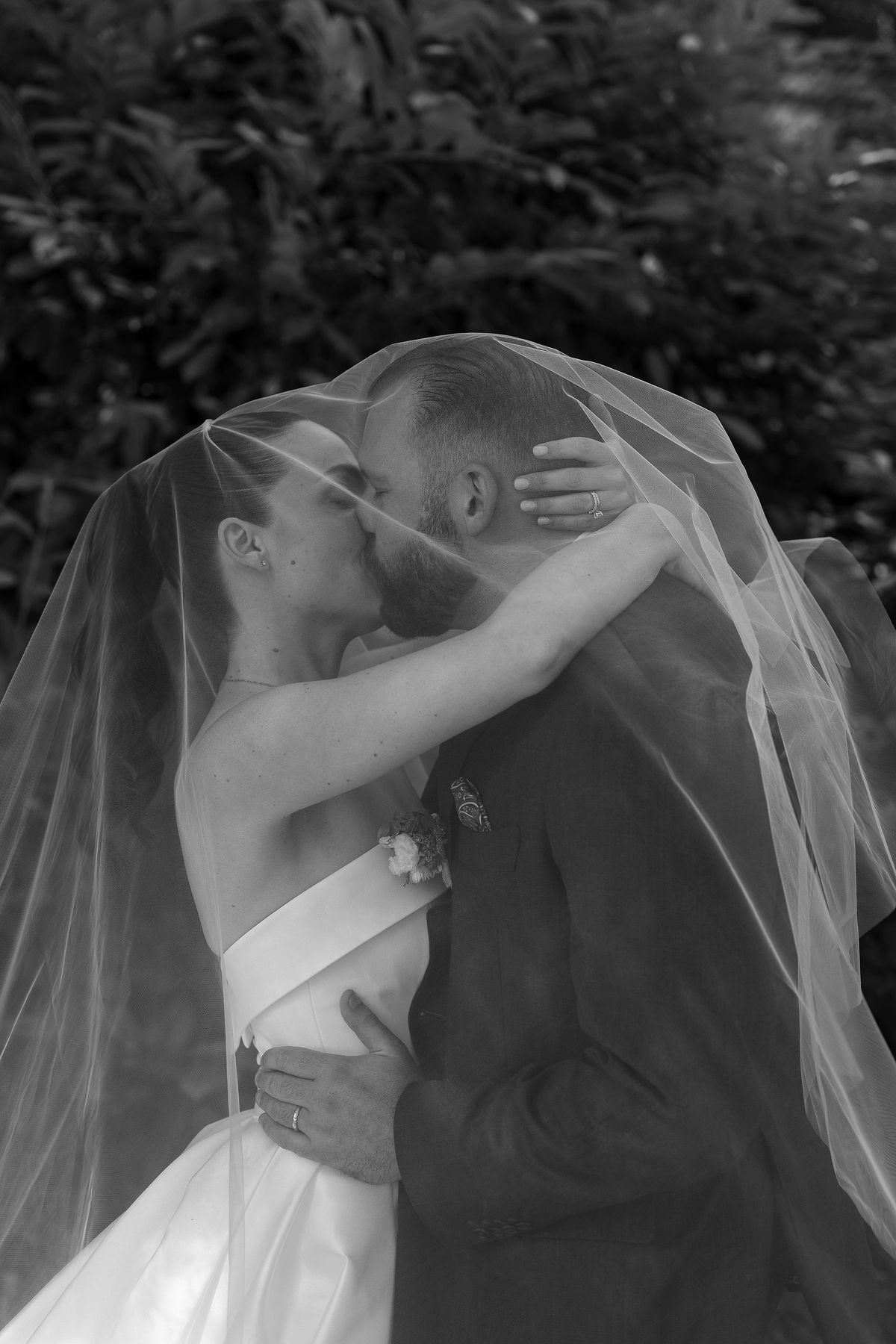 Black and white close image of the couple embracing and kissing while the bride's sheer veil drapes over them.