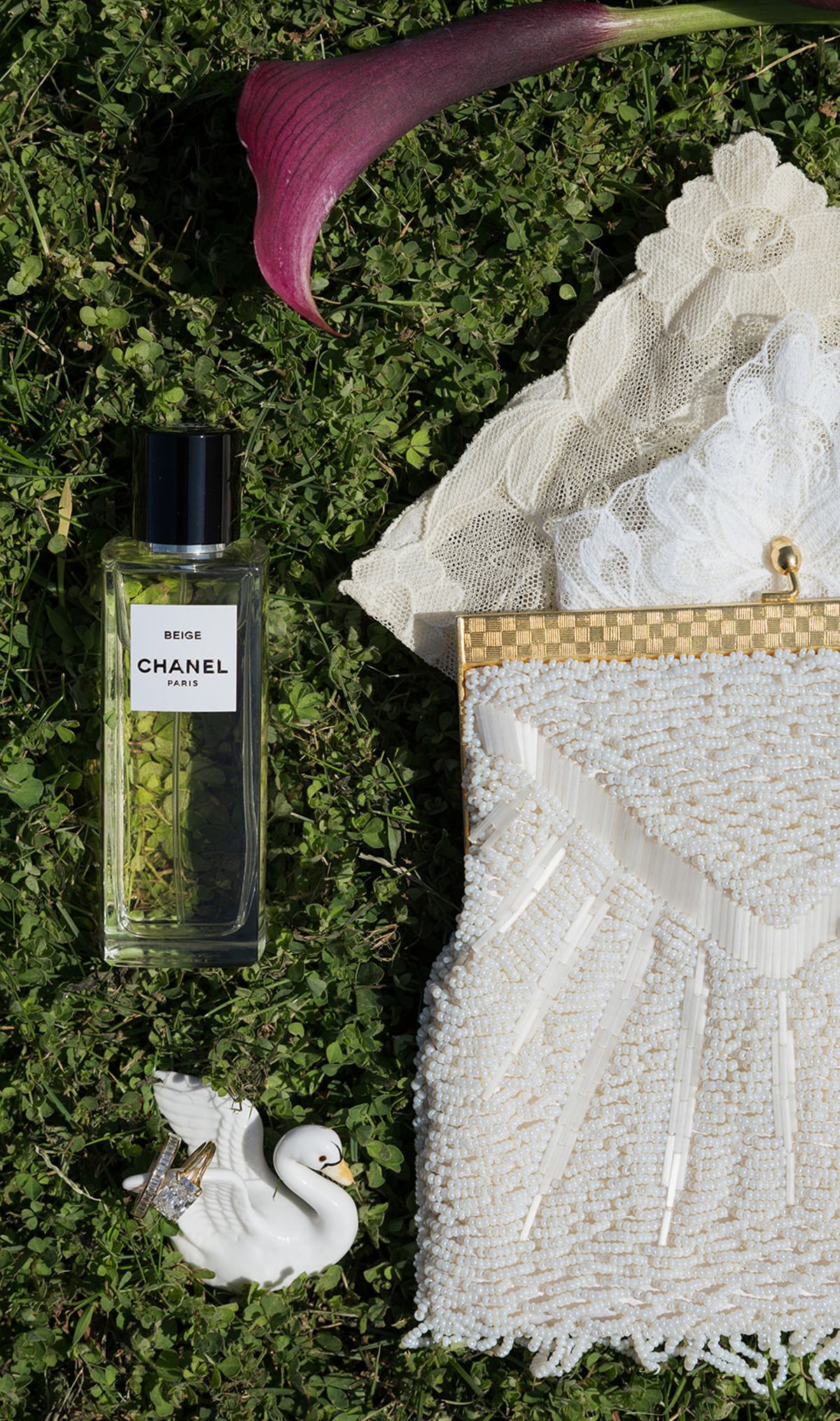 A beaded bridal bag, perfume and a ceramic swan laid on grass