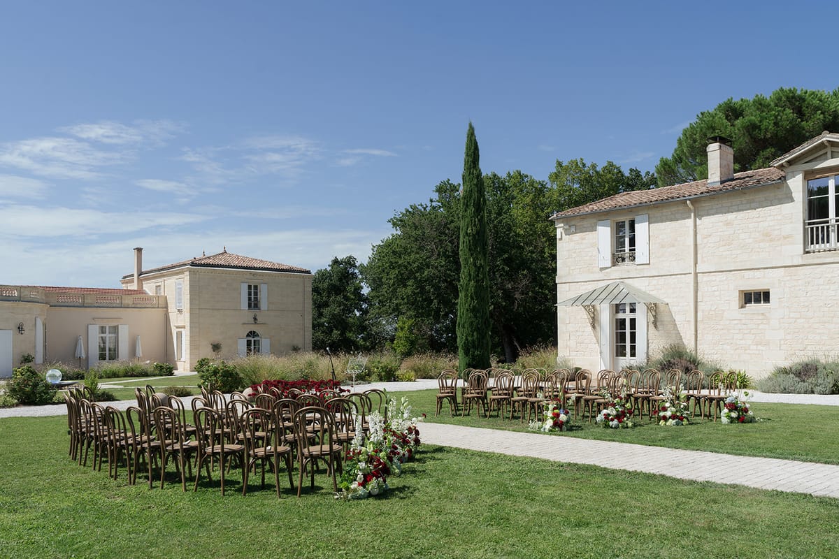 Bow-tie ceremony seating with red and white flowers on the lawn at Château Gassies