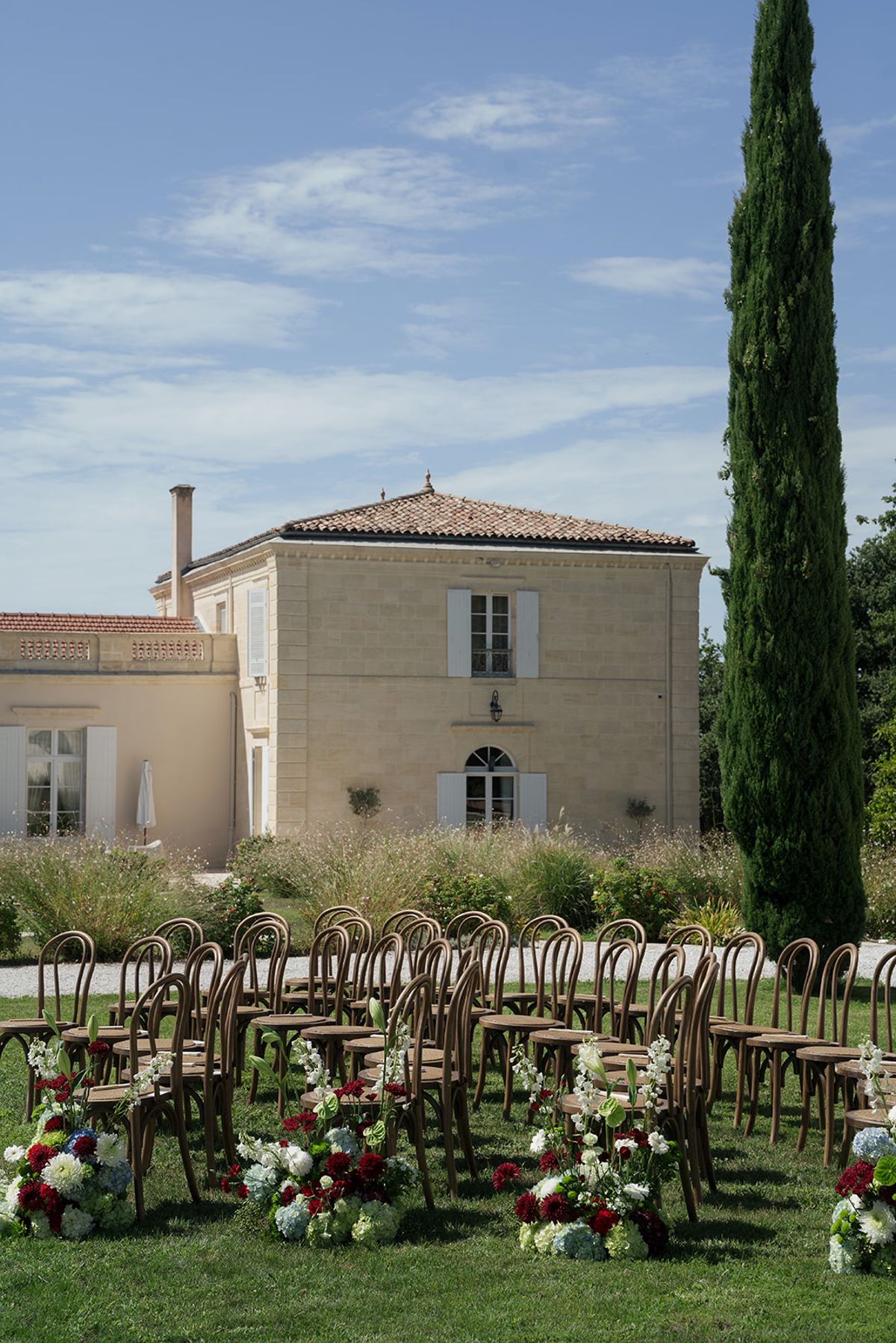 The pale stone façade of Château Gassies above the ceremony chairs and a tall cypress