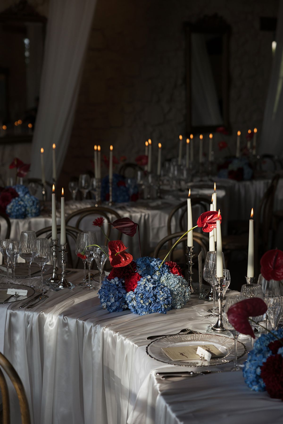A candlelit table with blue hydrangeas and red anthuriums