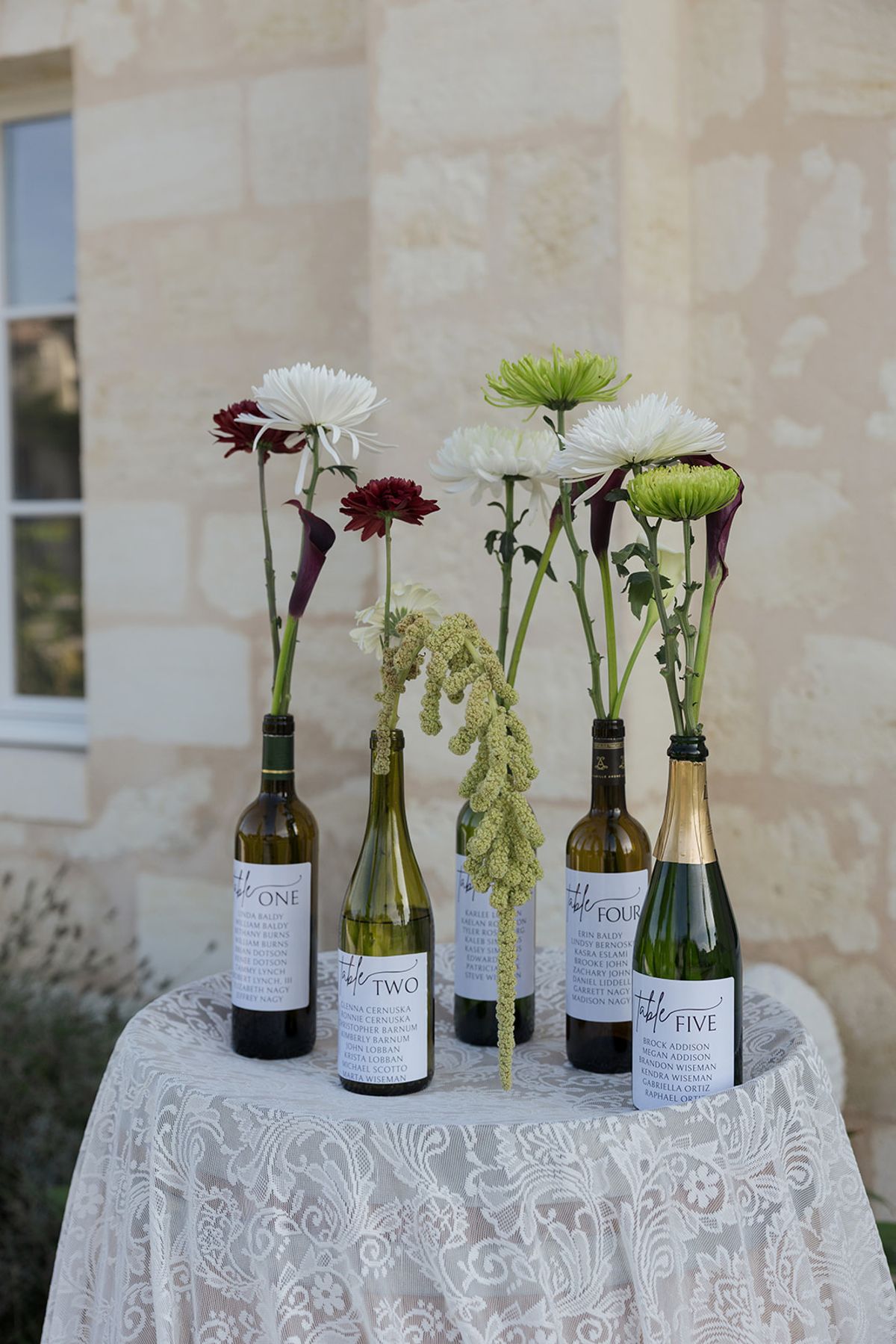 Wine bottles holding single stems on a lace-covered table