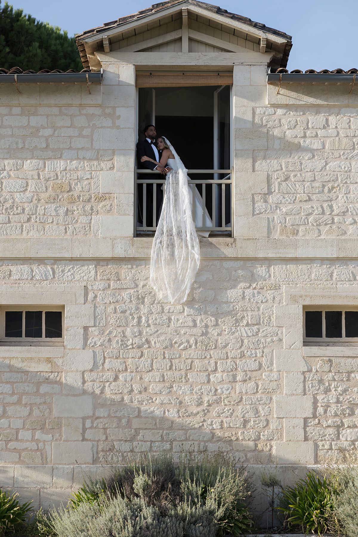 Kendra and Brandon at a railed upstairs opening, with her veil trailing down the stone wall