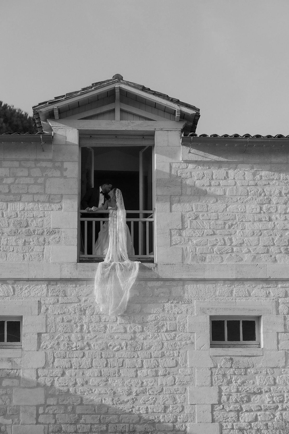 Kendra and Brandon at a railed upstairs opening, with her veil trailing down the stone wall, black and white