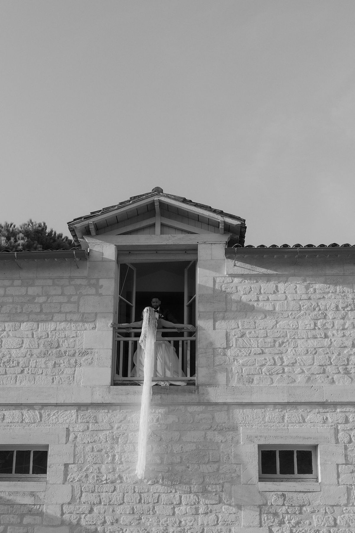 Kendra and Brandon at a railed upstairs opening, with her veil trailing down the stone wall, black and white
