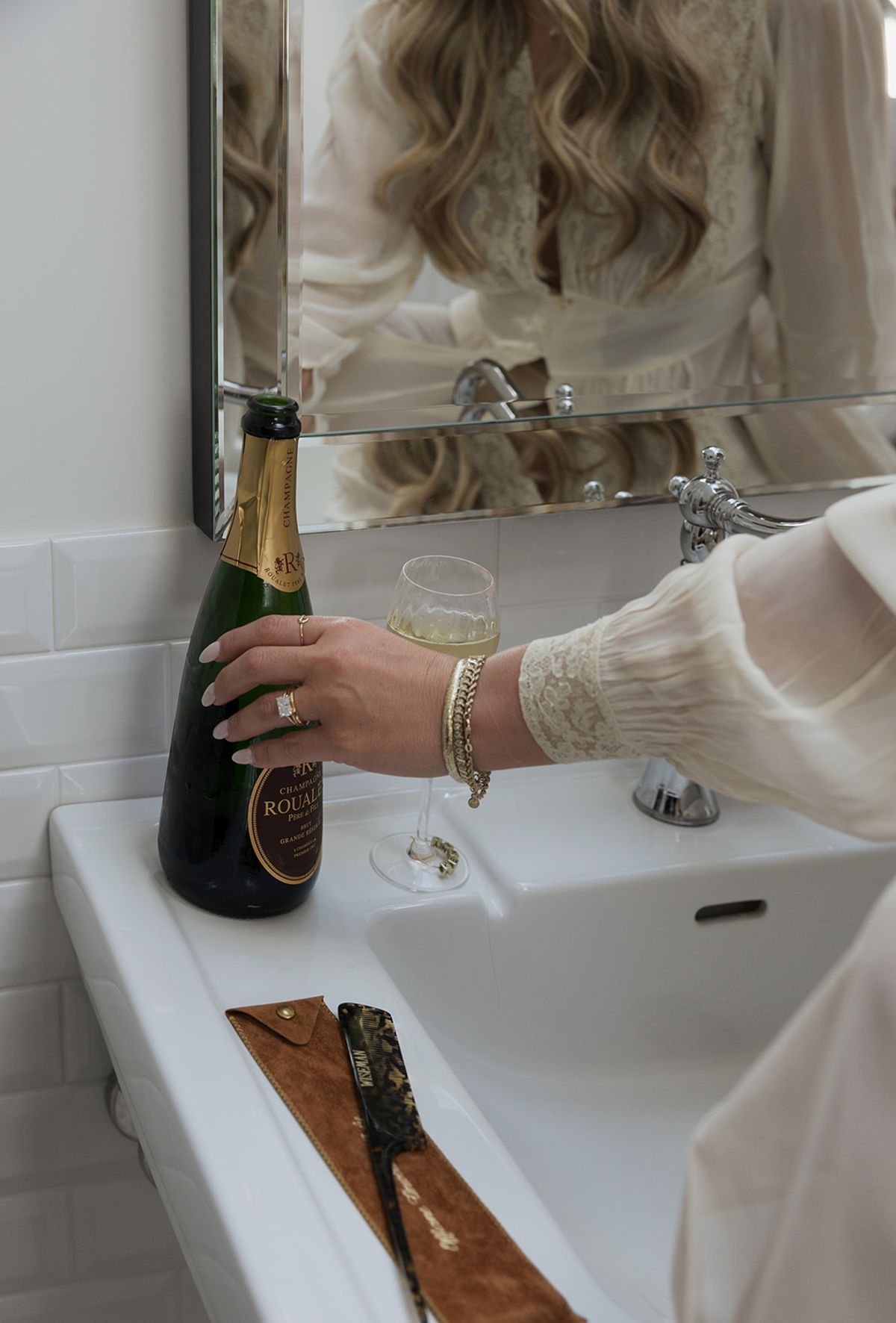A bottle of champagne beside the sink while Kendra gets ready