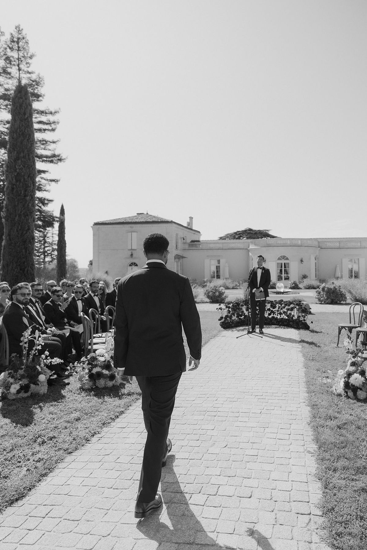 Brandon walking down the stone aisle between the guests, black and white
