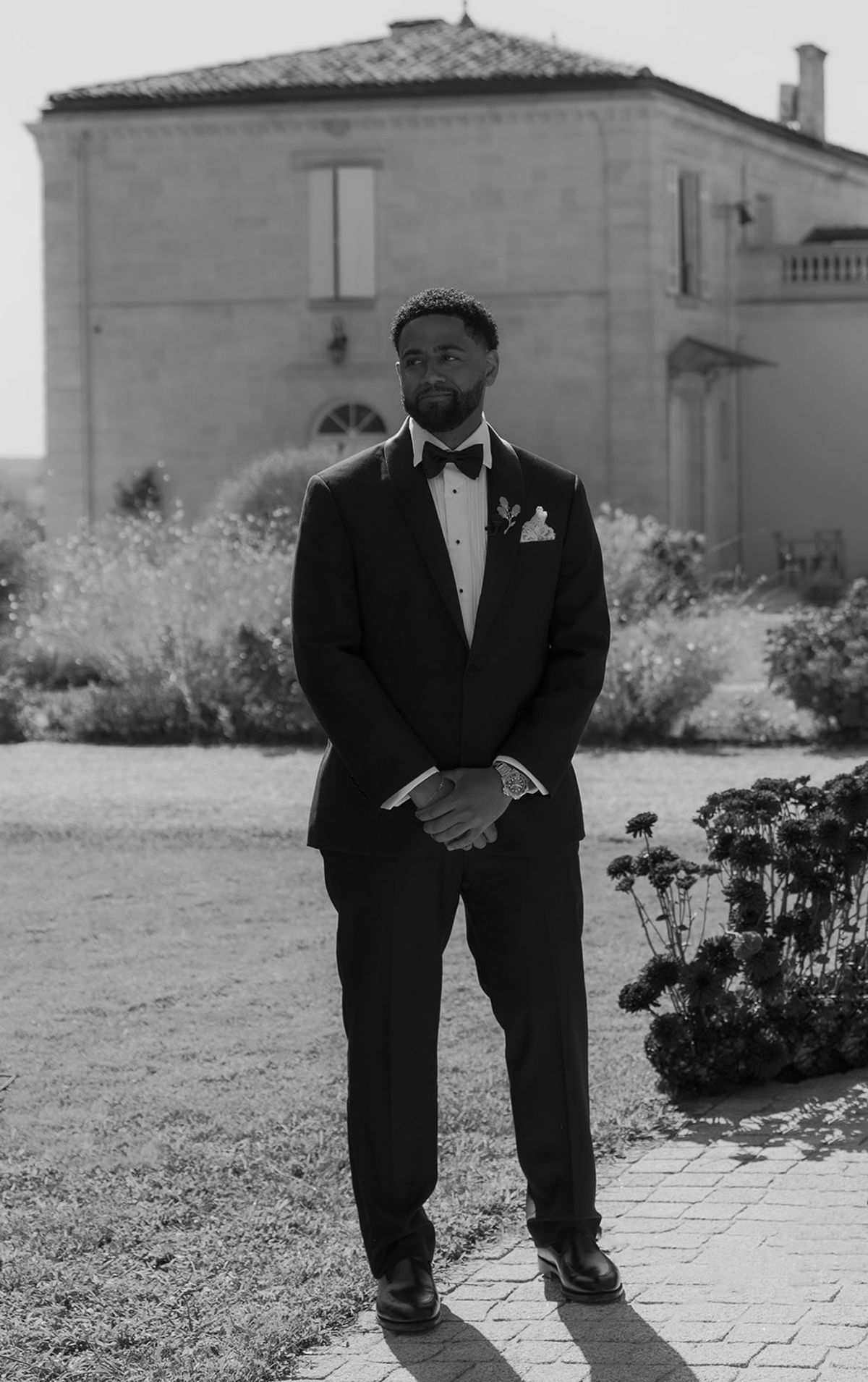 Brandon in a black tuxedo standing outside beside the ceremony seating