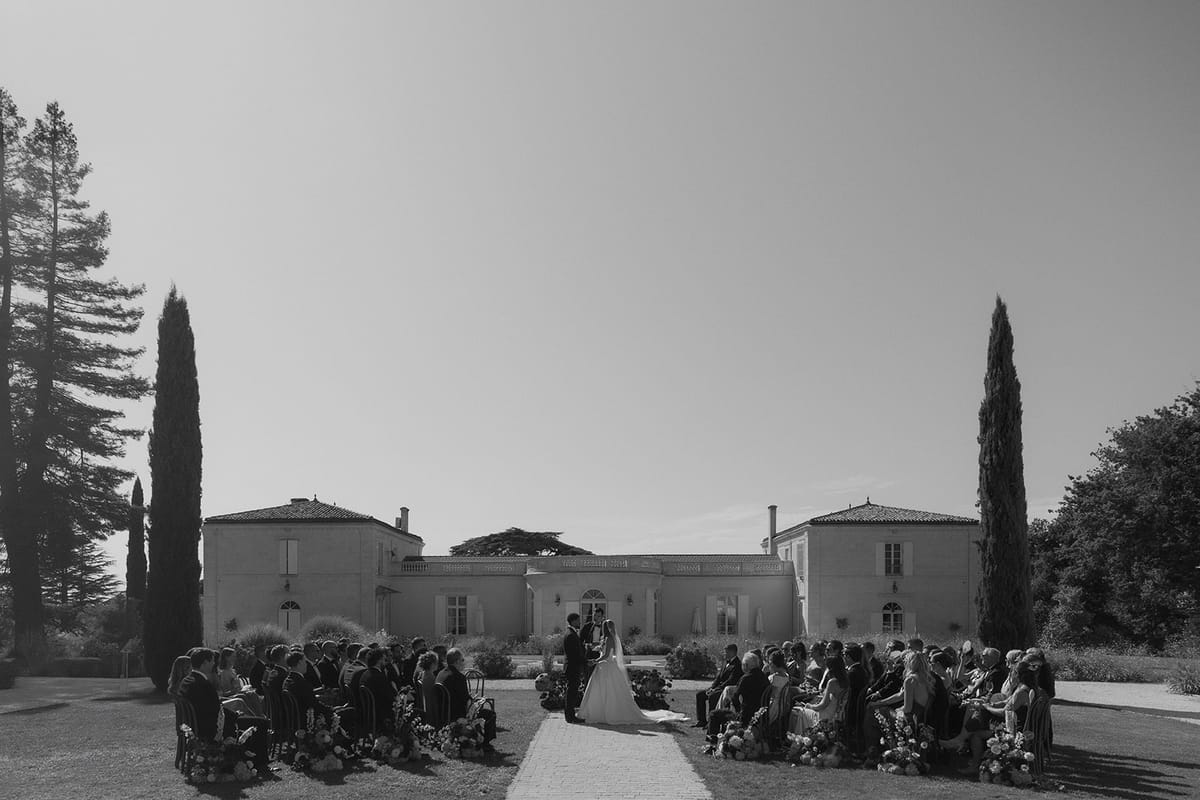 Wide view of the ceremony on the lawn at Château Gassies, black and white