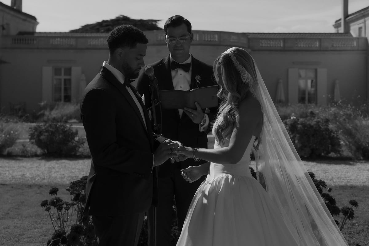 Kendra and Brandon exchanging rings with their officiant, black and white
