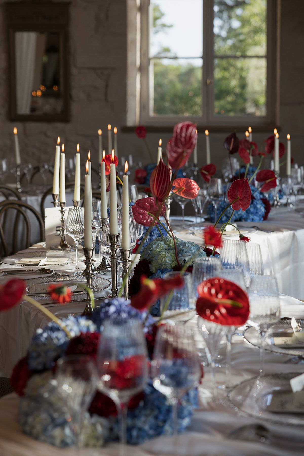 Red anthuriums and blue hydrangeas with tall candles on a dinner table