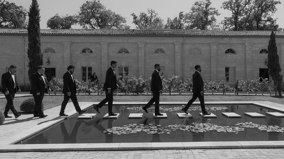 The groomsmen walking past the formal pond, black and white