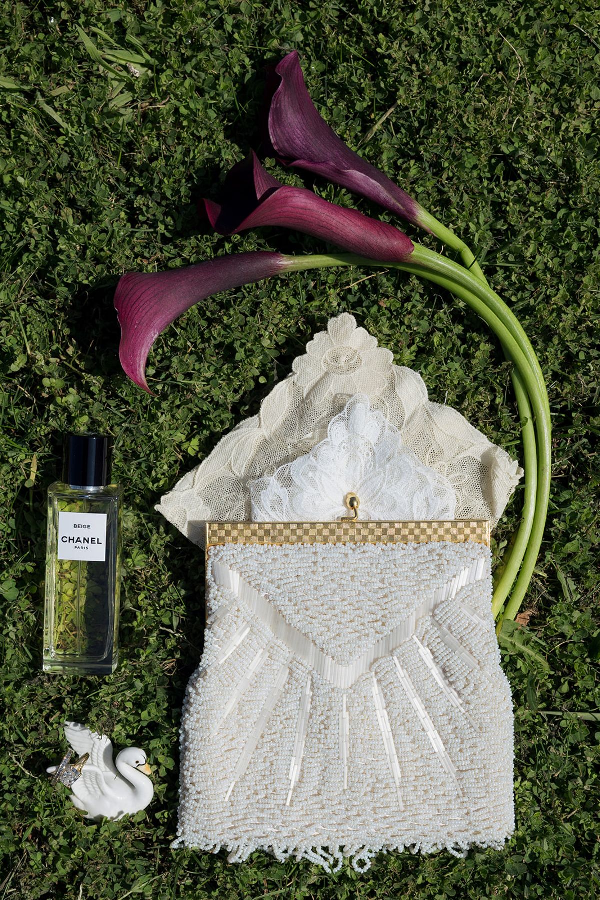 A beaded bridal bag, perfume and calla lilies laid on grass