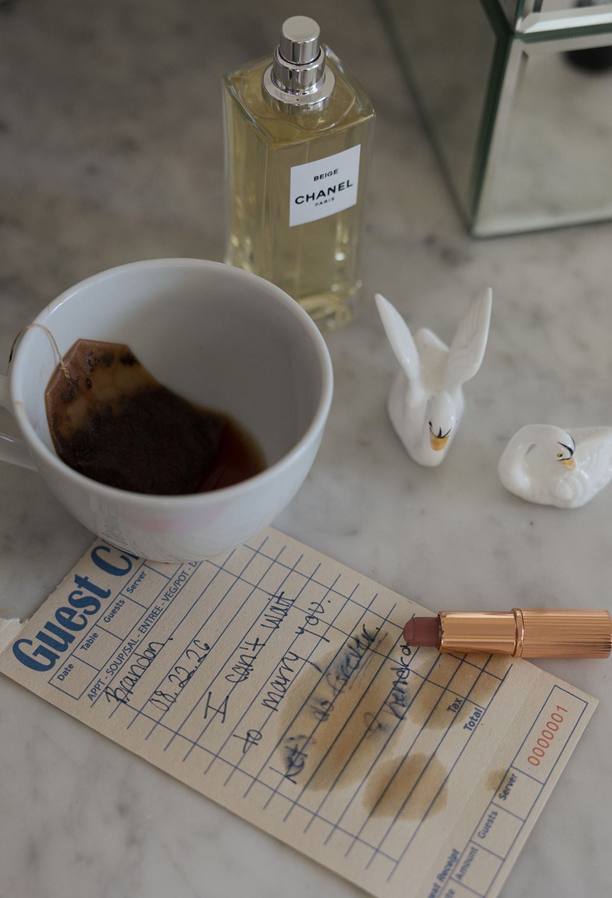 Perfume, a cup of tea and a handwritten guest check on marble