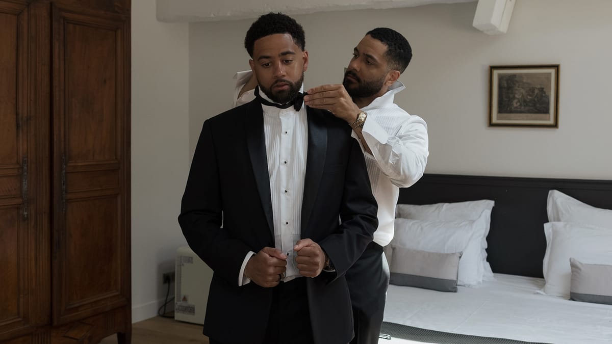 A groomsman helping Brandon with his bow tie