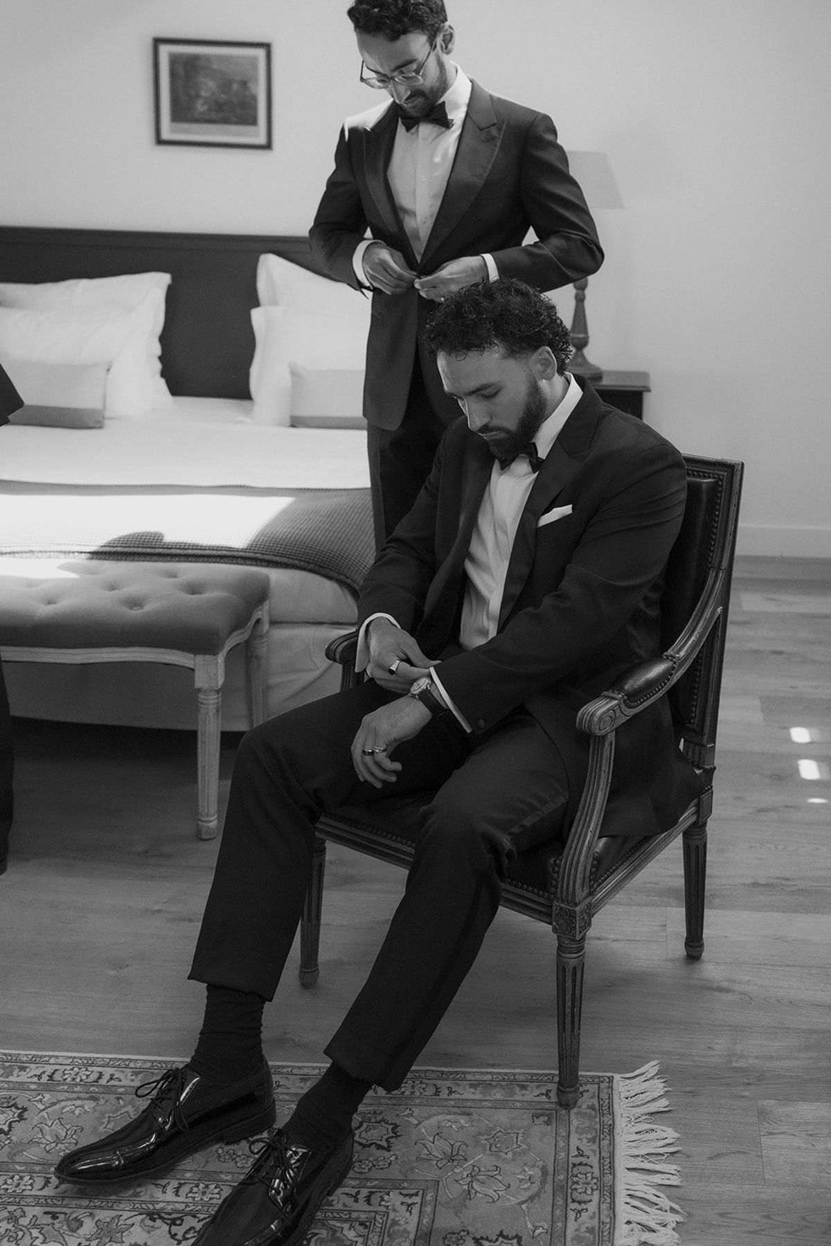 Brandon fastening his shoes while a groomsman adjusts his tie