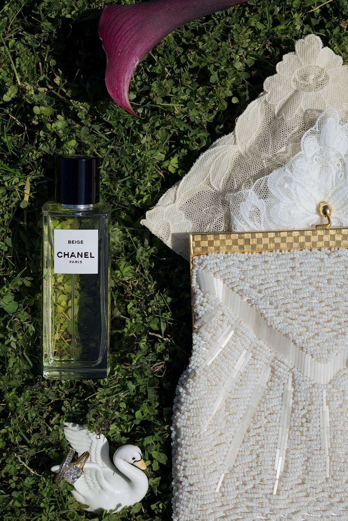 A beaded bridal bag, perfume and a ceramic swan laid on grass with a calla lily