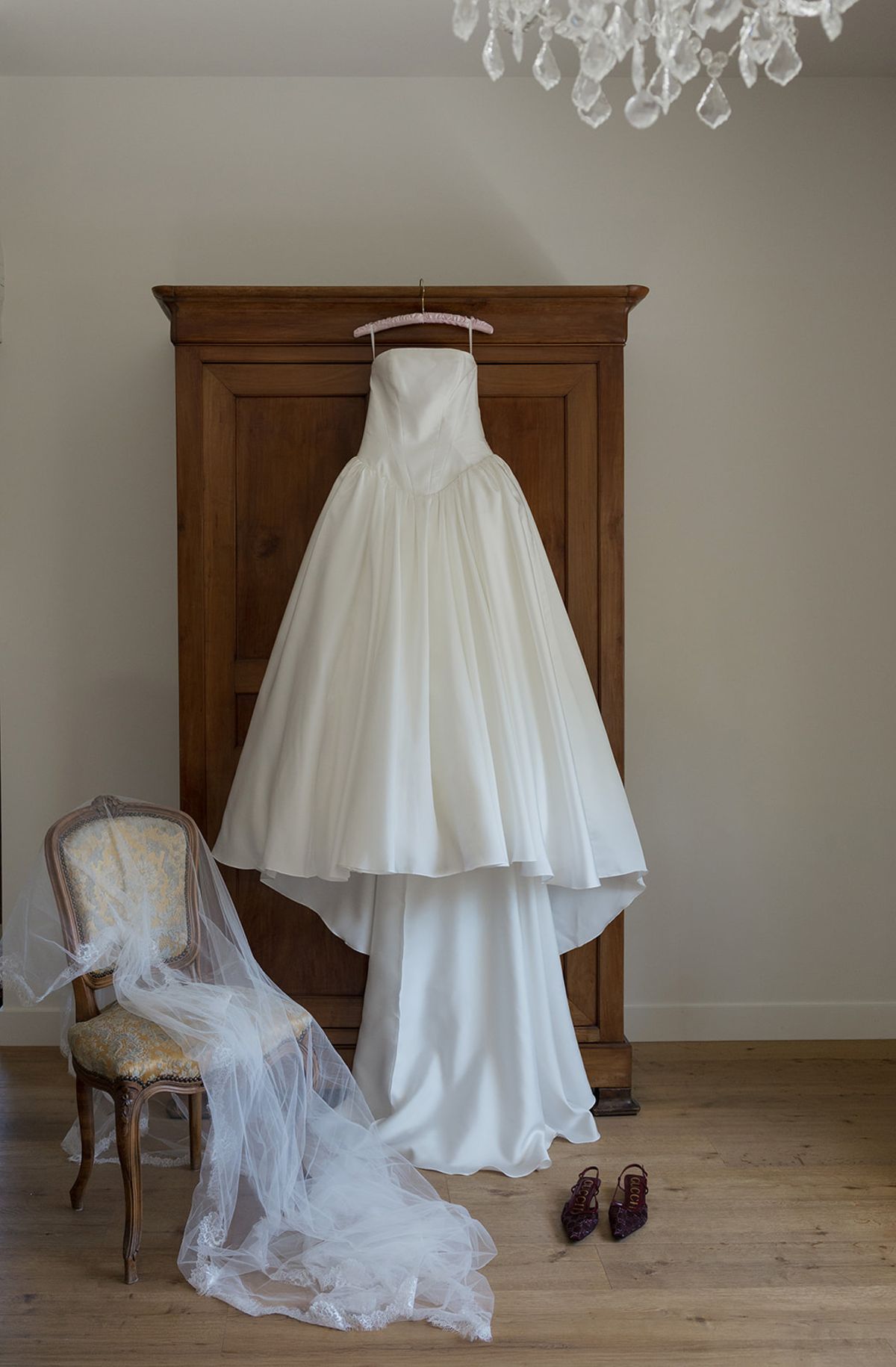 Kendra's gown hanging on a wooden armoire beside her veil and shoes