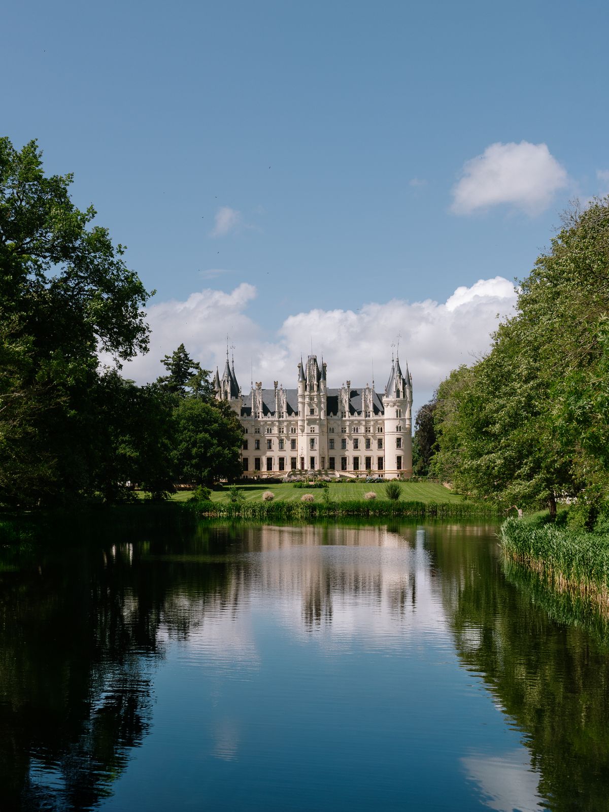 Chateau Challain reflected in the lake at the end of its tree-lined grounds