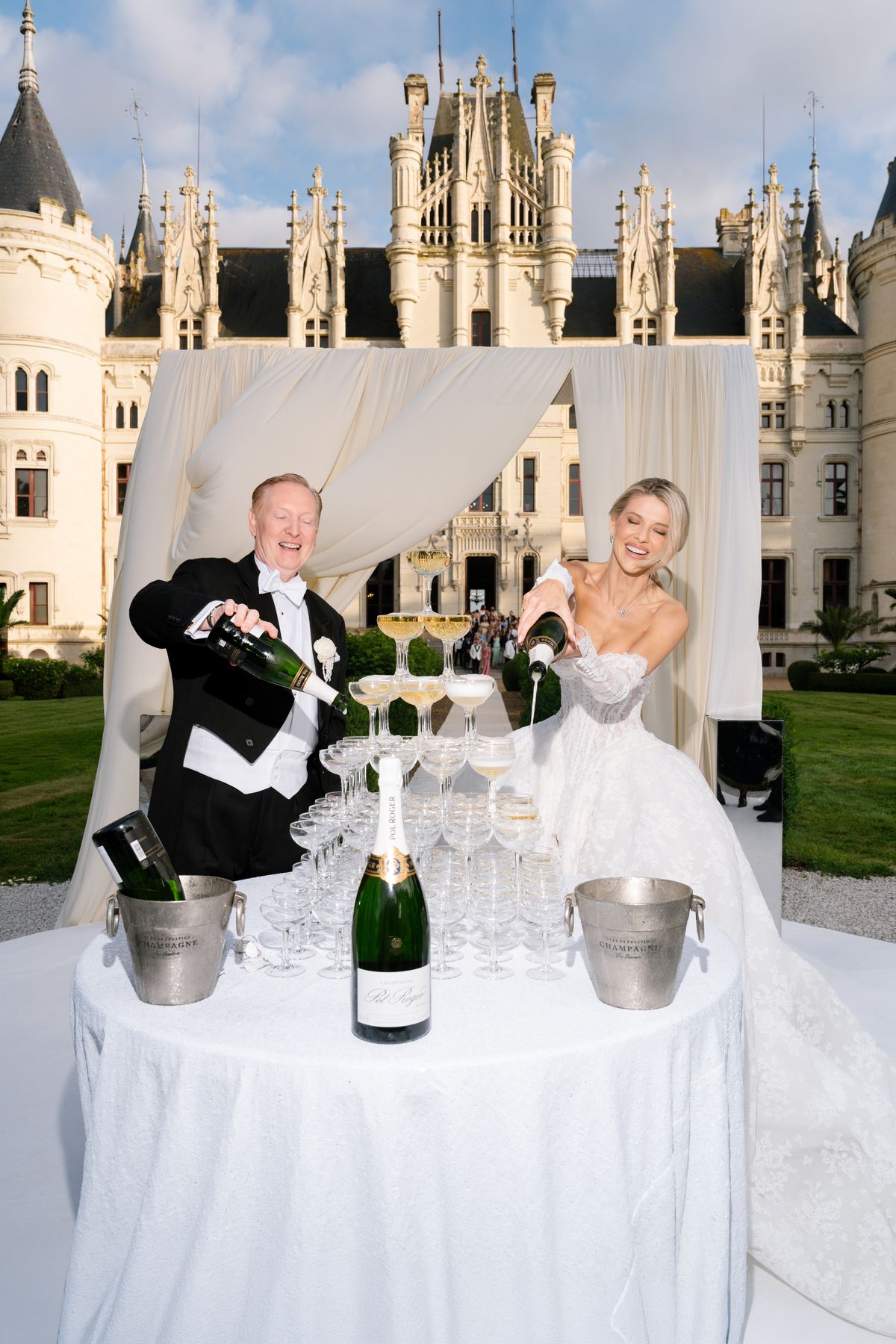Kira and Steve pour champagne over a coupe tower in front of Chateau Challain