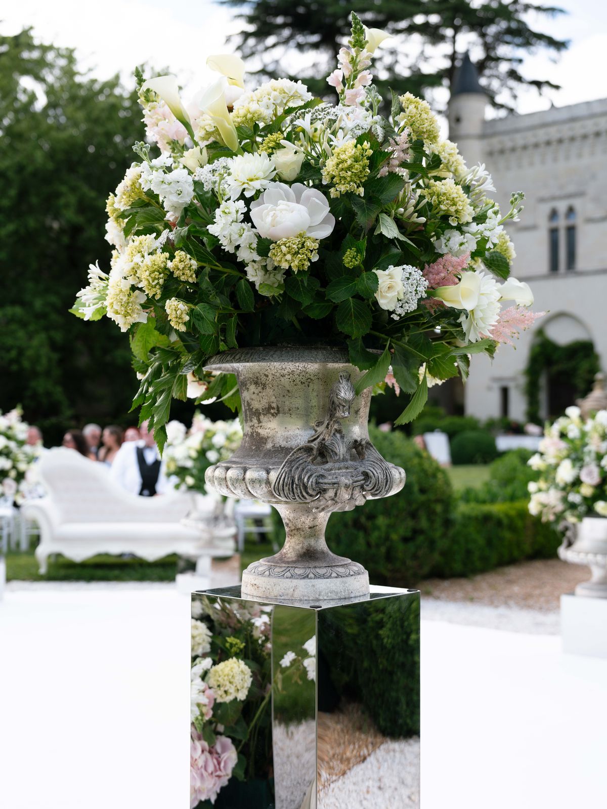 A silver urn of white and green flowers on a mirrored plinth beside the ceremony aisle
