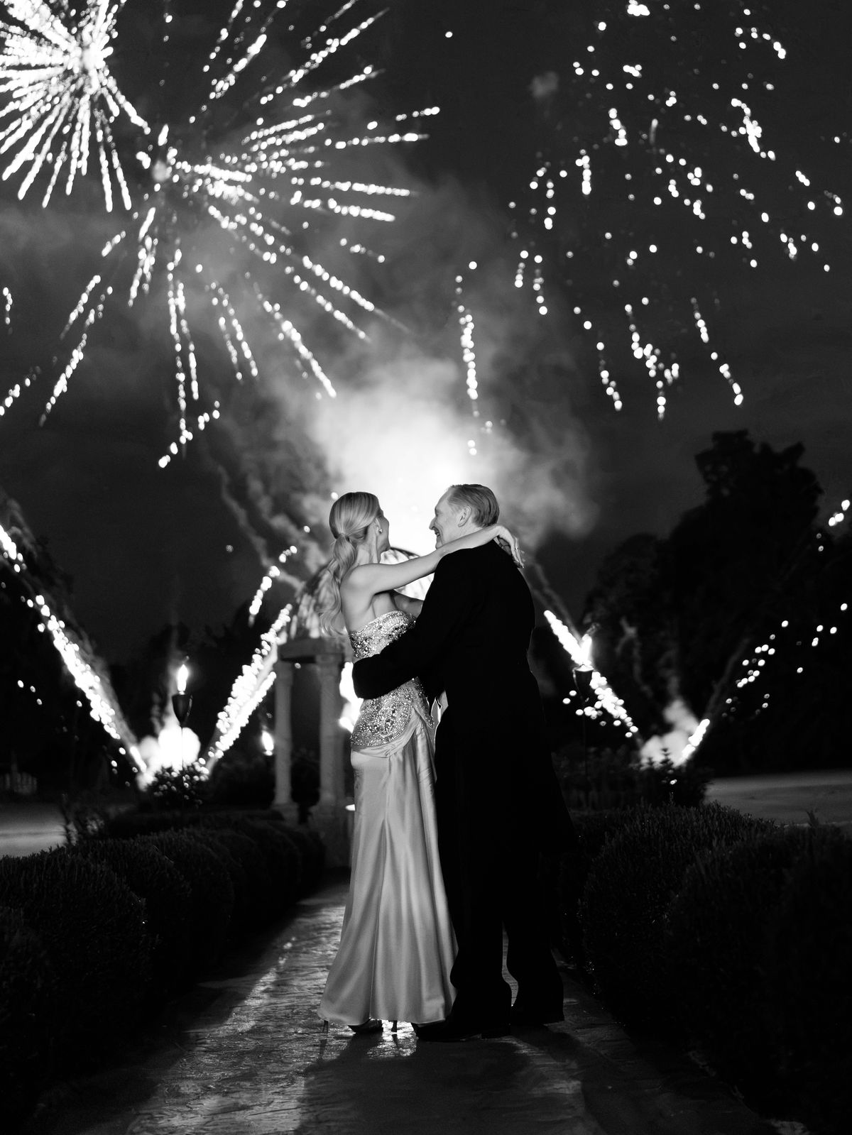 Kira and Steve embrace on the garden path as fireworks light the sky at Chateau Challain