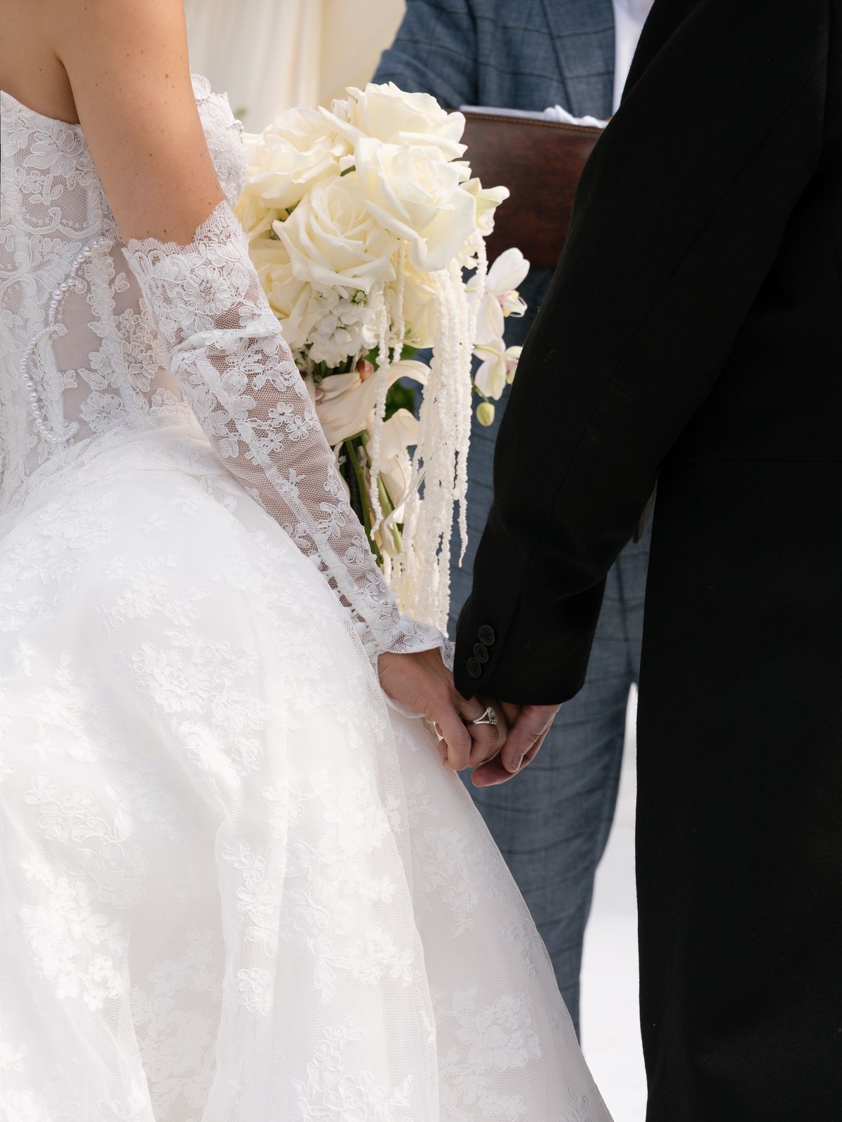 Kira and Steve hold hands during the ceremony, Kira carrying a white orchid bouquet