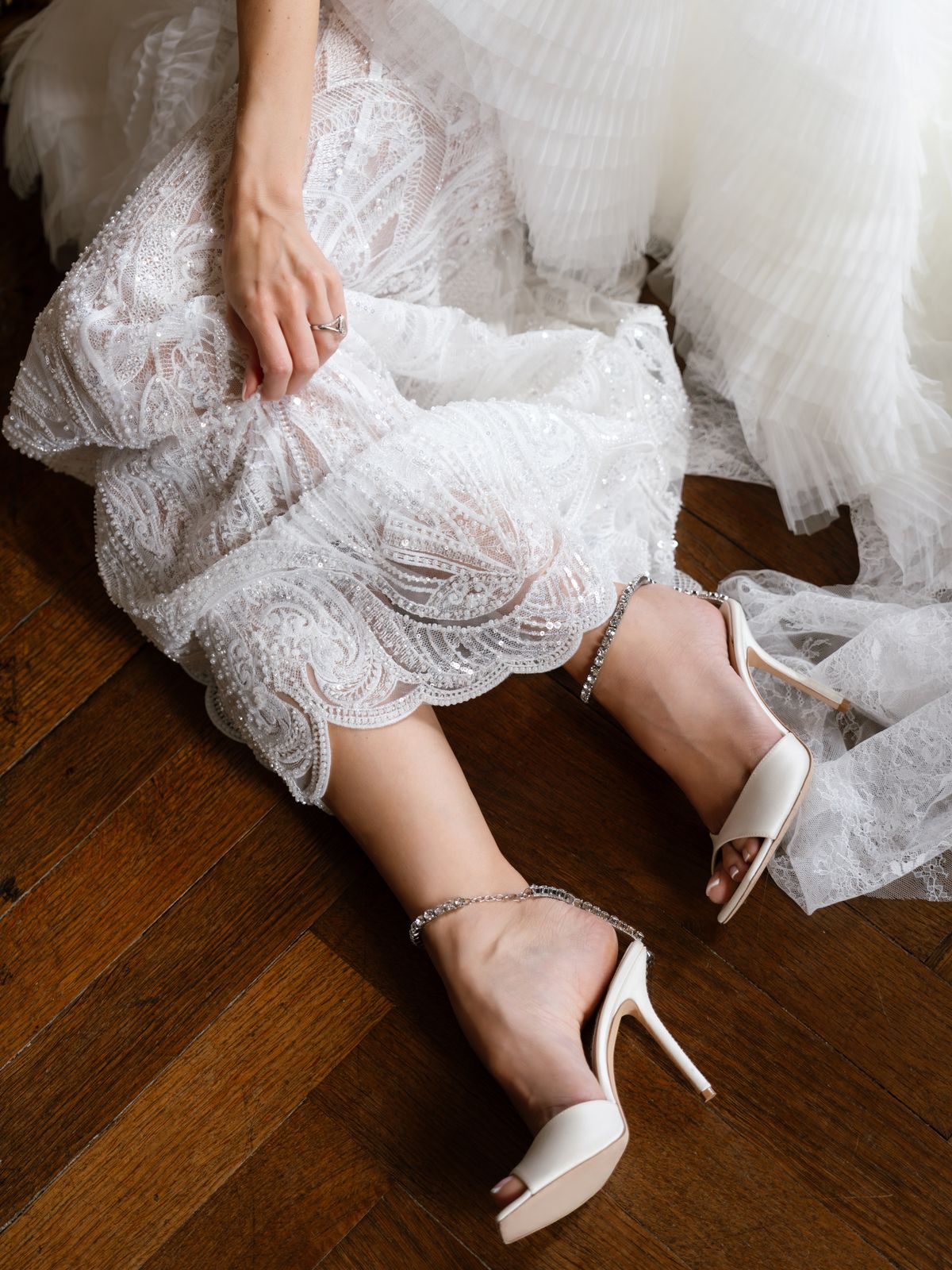Kira's white satin heels beneath her pearl-embroidered skirt on a parquet floor