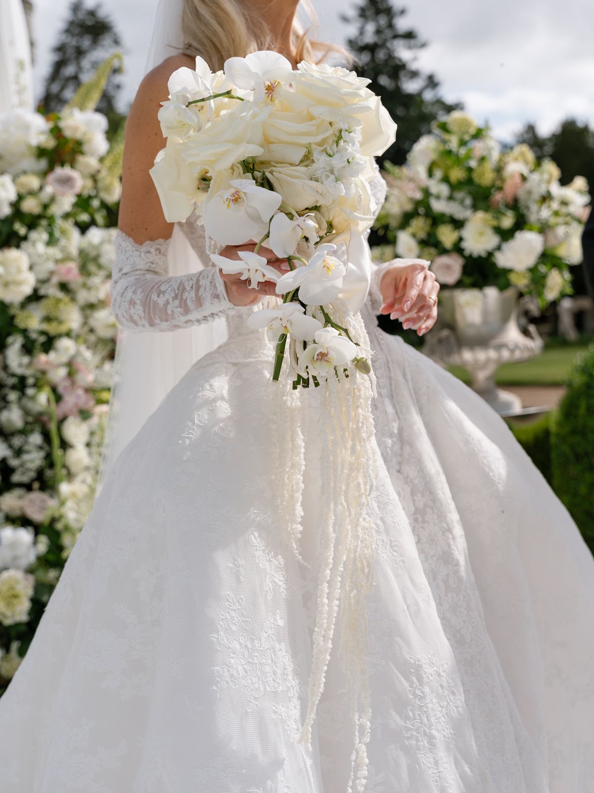Kira's white rose and orchid bouquet held against her lace gloves and gown