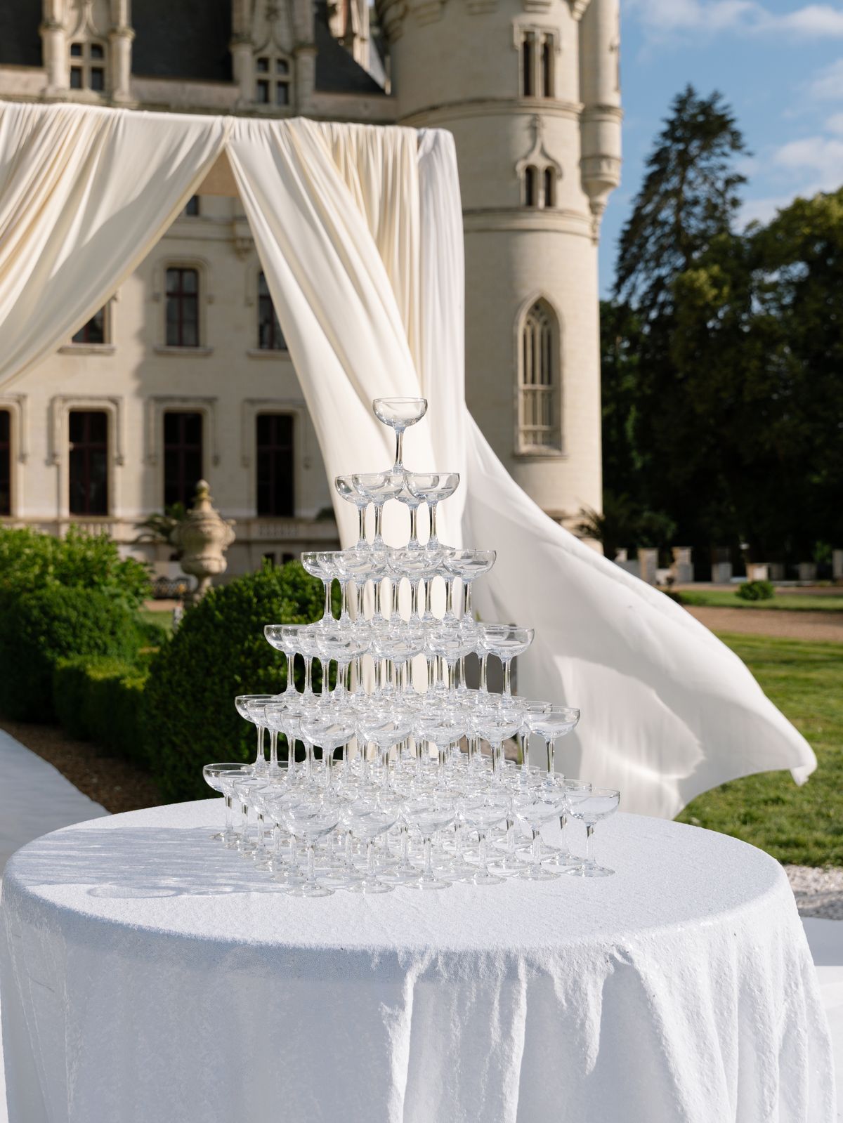 A champagne coupe tower beside billowing drapes in front of Chateau Challain