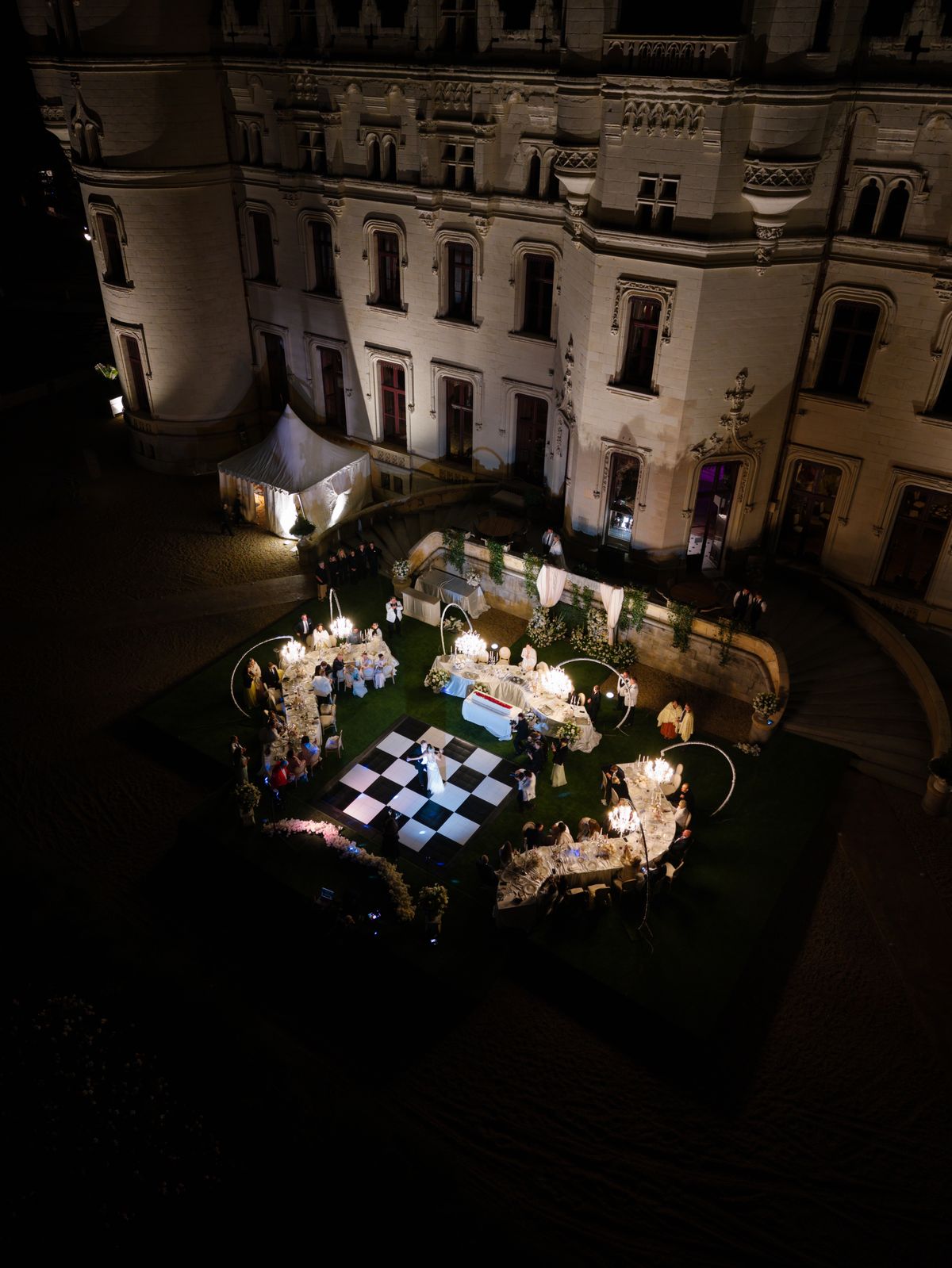 Night aerial view of the lit dinner tables and dance floor in the courtyard of Chateau Challain