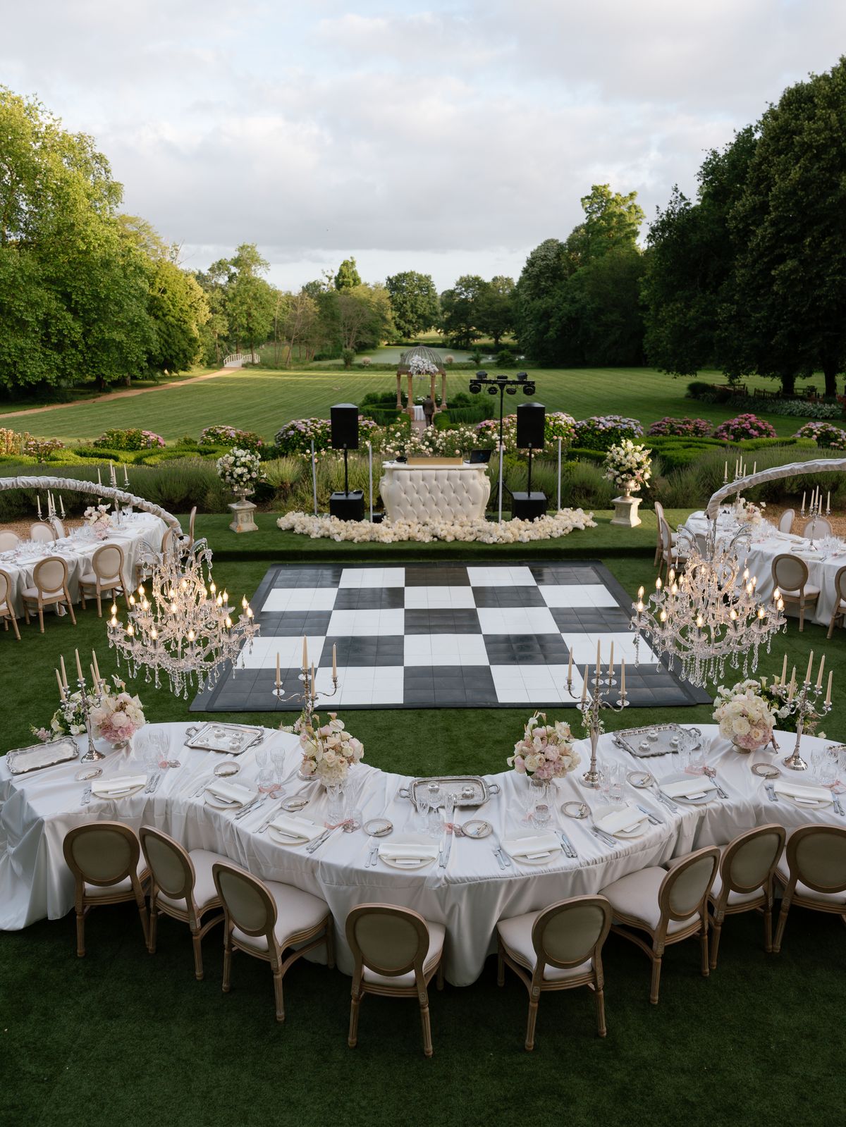 Dinner tables under crystal chandeliers around a checkerboard dance floor on the lawn at Chateau Challain