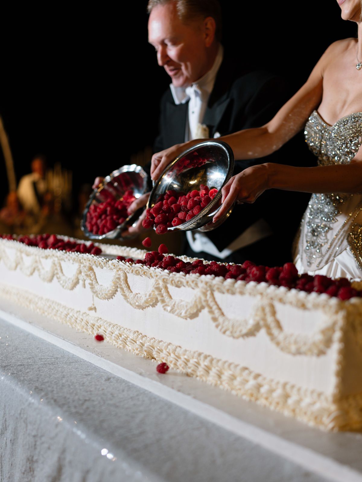 Kira and Steve pour raspberries over the long wedding cake during the cake cutting
