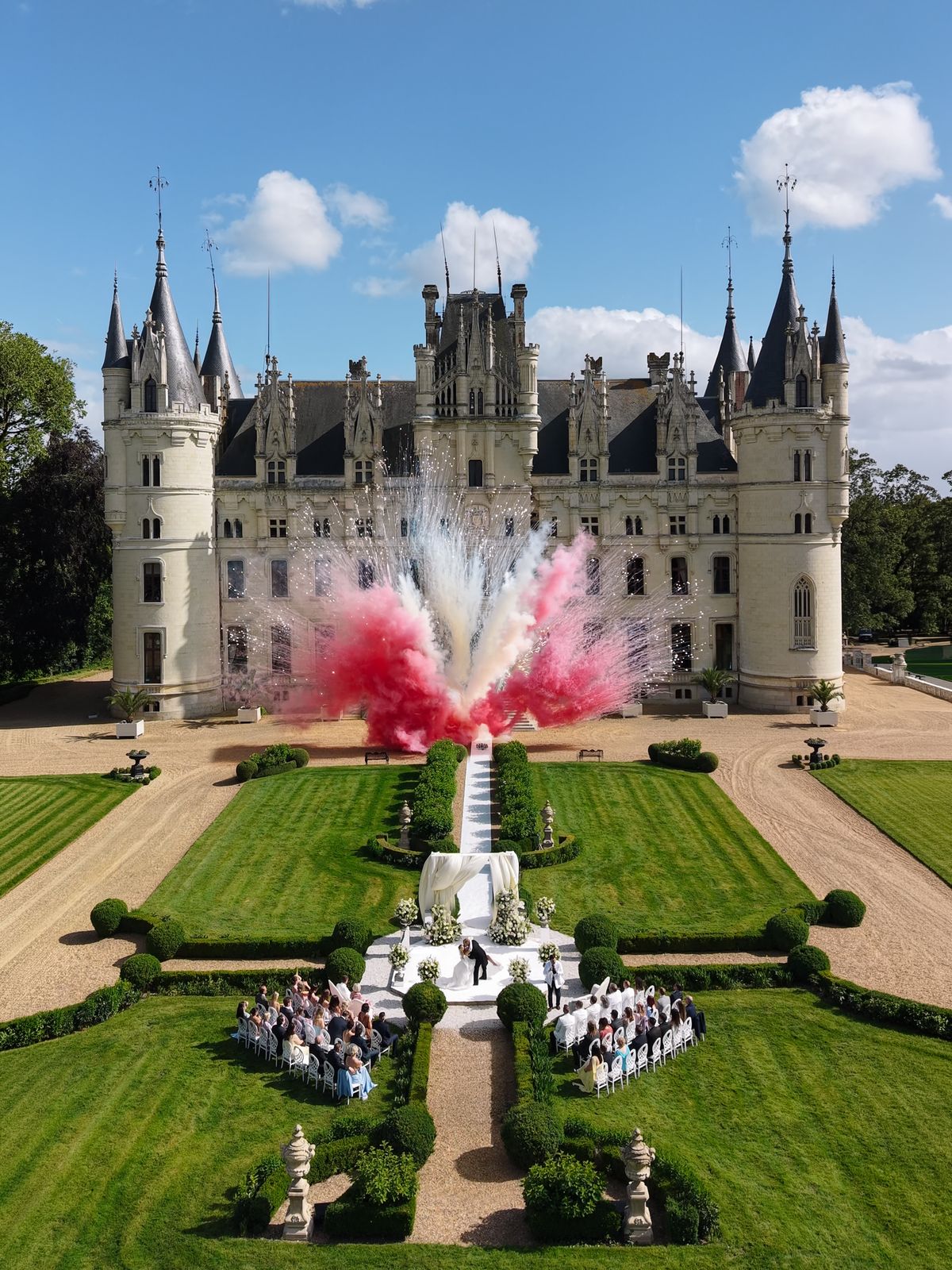 Aerial view of pink and white colour smoke rising over the ceremony in front of Chateau Challain
