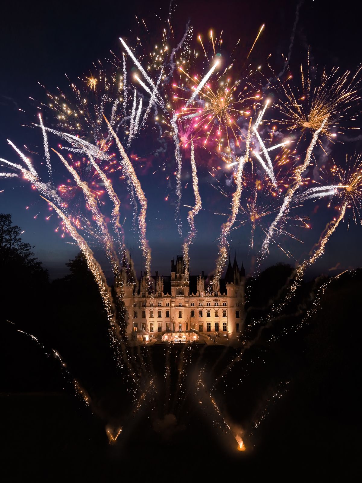 Fireworks burst over the illuminated facade of Chateau Challain at night