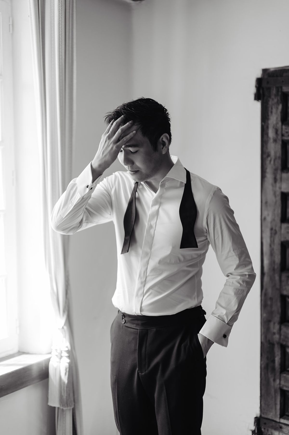 Ruiji adjusting his bow tie by the window, black and white