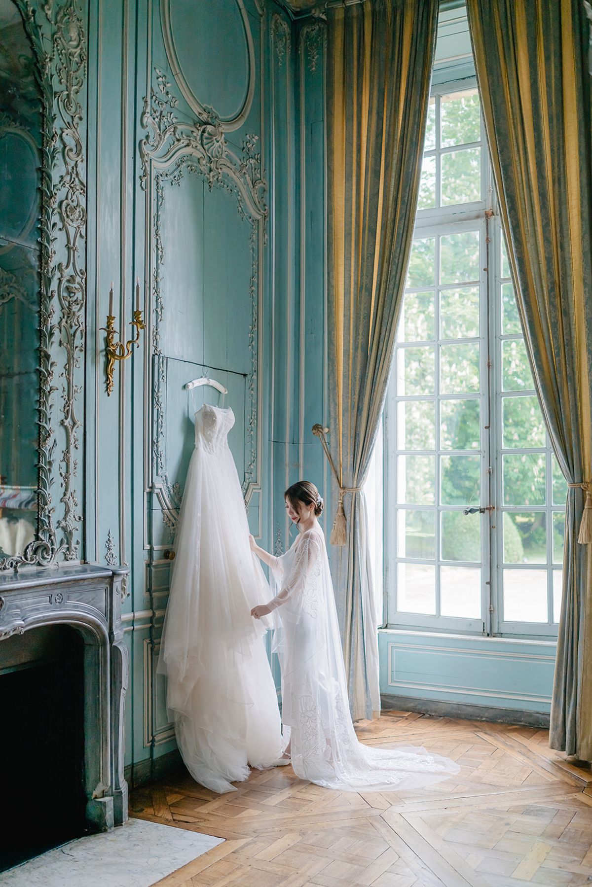 Liana alone by a tall window in the bridal suite before the ceremony