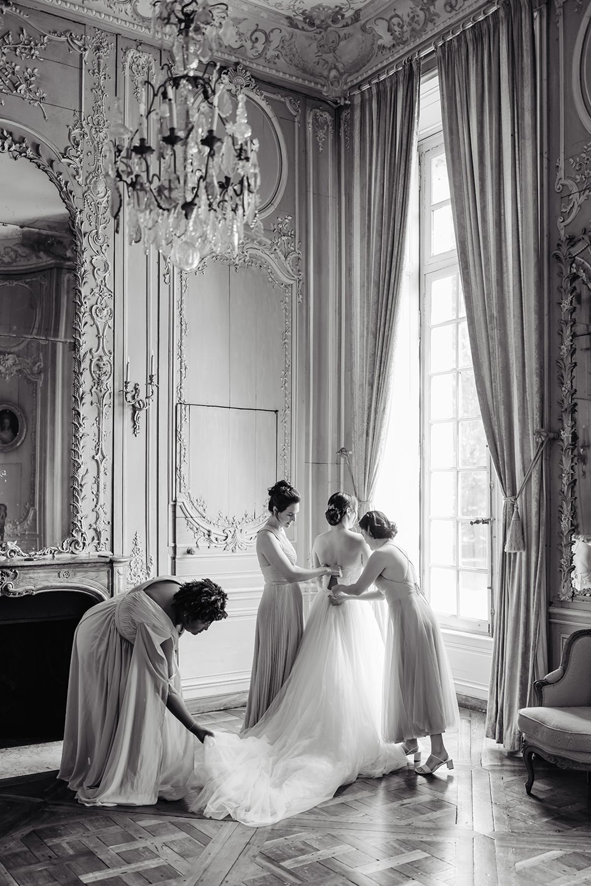 Liana having her dress fastened by her bridesmaids, black and white