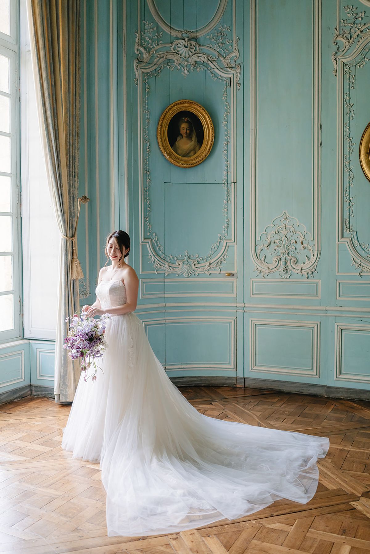Liana standing for a formal portrait in the blue panelled room, holding her bouquet