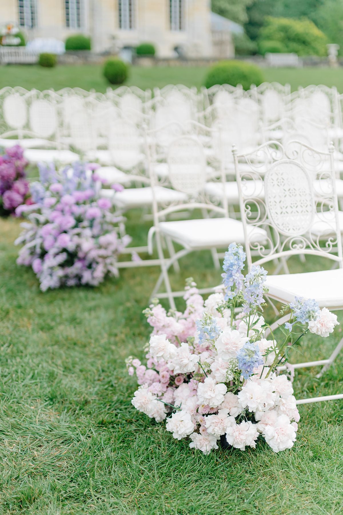 Empty ceremony aisle chairs lined with lilac and white floral arrangements