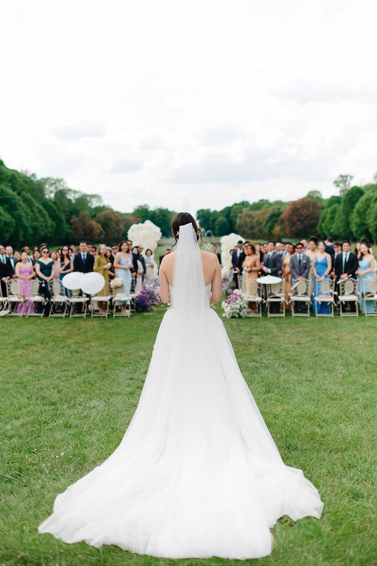 Liana walking down the aisle toward the seated guests at Château de Champlâtreux