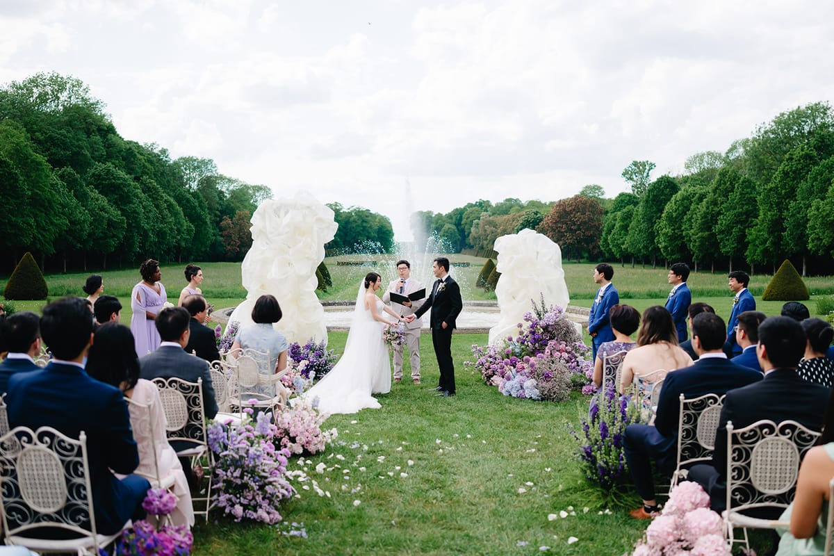Liana and Ruiji exchanging vows in front of the garden fountain, guests seated either side